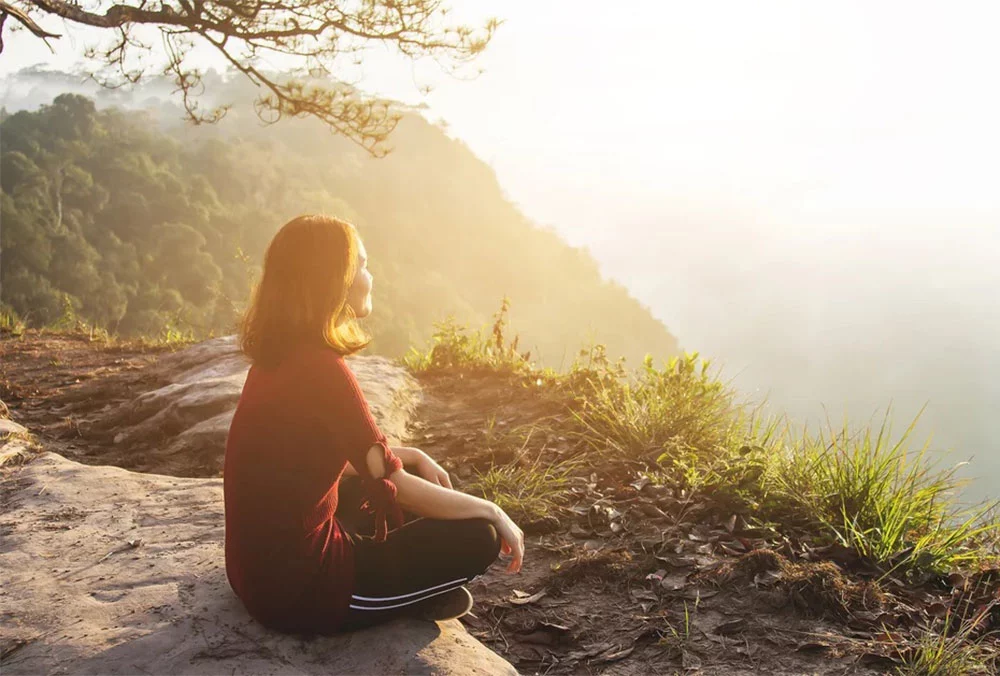 Person practicing mindful breathing in a calm natural setting with soft morning light